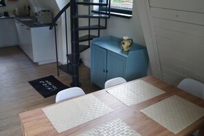 A dining area with a wooden table, white chairs, a blue cabinet, and a black spiral staircase. - Lake Bieszkowice Holiday Cabin (Bieszkowice)