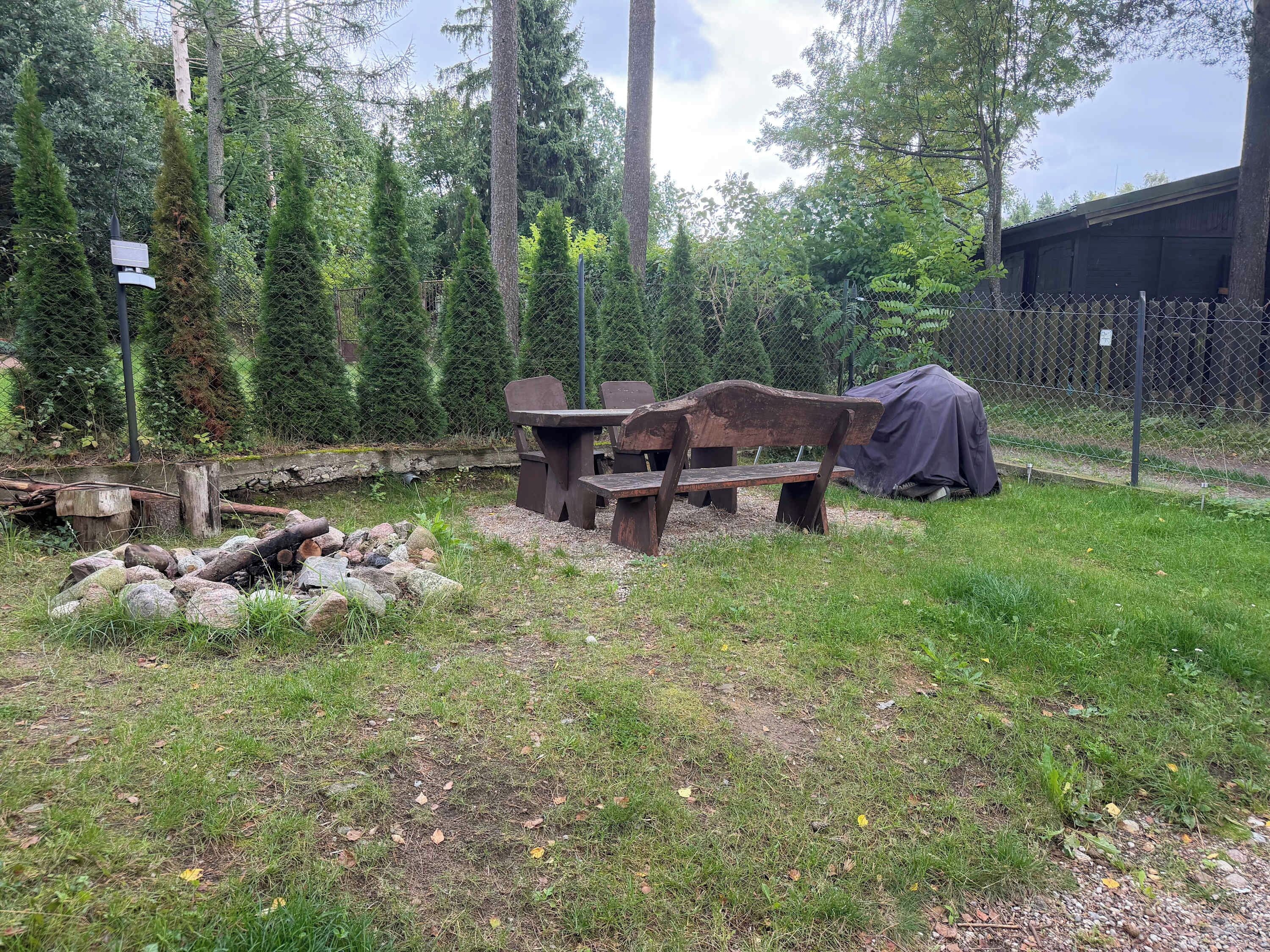 An outdoor seating area with a picnic table and benches, surrounded by a fence and trees.