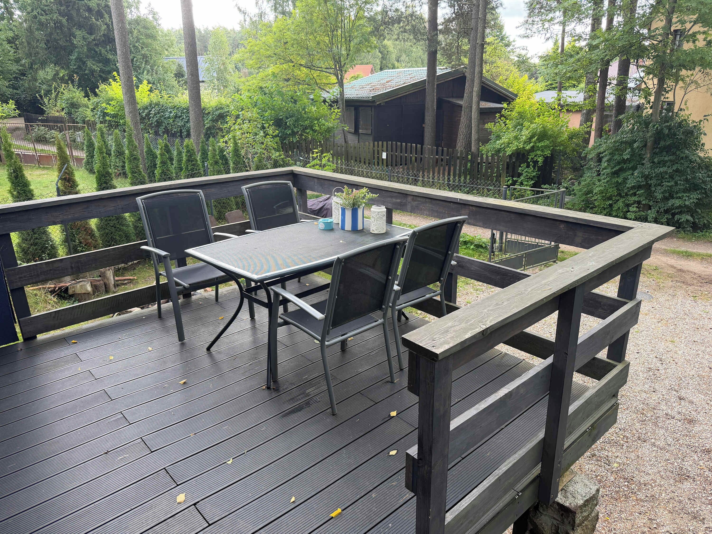 A deck with a table and chairs, surrounded by a wooden fence and trees.