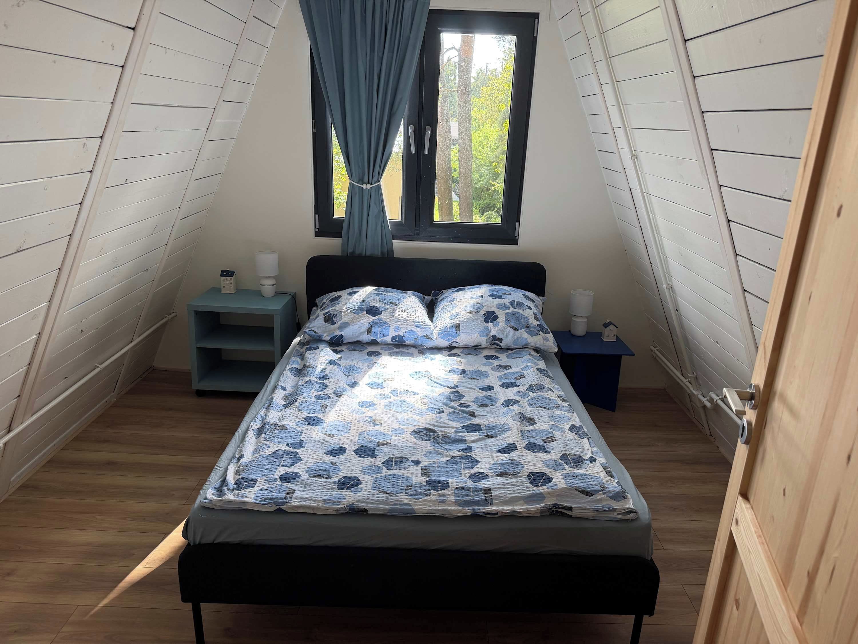 A bedroom with a bed, a nightstand, a window with curtains, and a small table.