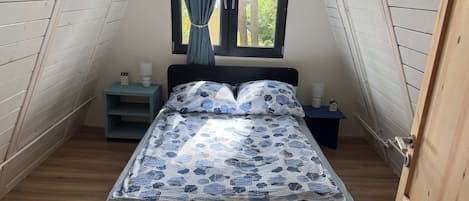 A bedroom with a bed, a nightstand, a window with curtains, and a small table.