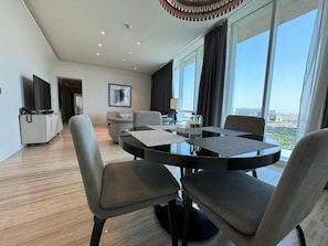 A modern hotel room with a round dining table, four chairs, a flat-screen TV, and a large window offering a city view. - Hotel Suites - Damac Tower Riyadh (Riyadh)