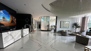 A spacious lobby with a marble floor, a reception desk, seating areas, and a large chandelier. - Hotel Suites - Damac Tower Riyadh (Riyadh)
