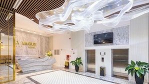 A hotel reception area with a marble reception desk, a large chandelier, and potted plants. - La Vague Hotel (Nha Trang)