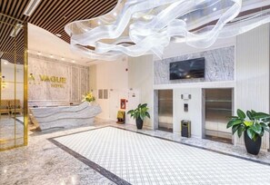 Un hall d’hôtel avec un comptoir d’accueil en marbre, un grand lustre et des plantes en pot.