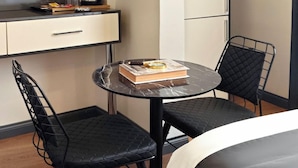 Une petite pièce avec un lit, une table ronde et deux chaises, un livre et une loupe posés sur la table.