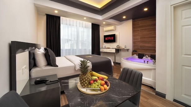 Une chambre d’hôtel moderne équipée d’un lit, d’un coin repas avec des fruits, d’une télévision et d’un jacuzzi.