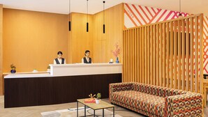 A reception area with a wooden reception desk, two receptionists, a patterned sofa, a small table with a vase, and a decorative wall panel. - Ginger Nagpur City Centre (Nagpur)