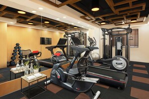 Ein Fitnessraum mit Laufbändern, Crosstrainern, einer Gewichtbank und Kurzhanteln.