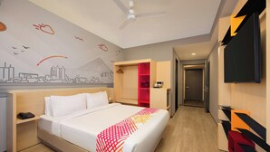 A hotel room with a bed, a desk, a telephone, a red storage unit, and a television on the wall. - Ginger Nagpur City Centre (Nagpur)
