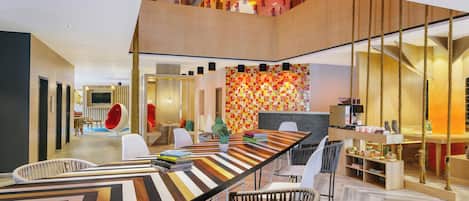 A modern interior with a long dining table, multiple seating options, and a staircase leading to an upper level.