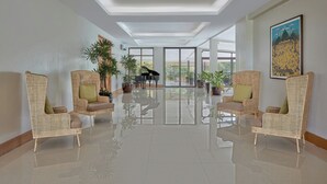 A spacious lobby with a piano, wicker chairs, and potted plants. - Holiday Inn & Suites Batangas Limapark (Malvar)