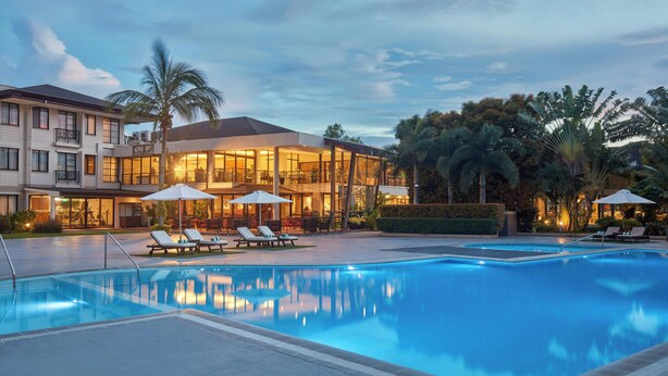 A swimming pool with lounge chairs and umbrellas, surrounded by a building with multiple floors and balconies. - Holiday Inn & Suites Batangas Limapark (Malvar)