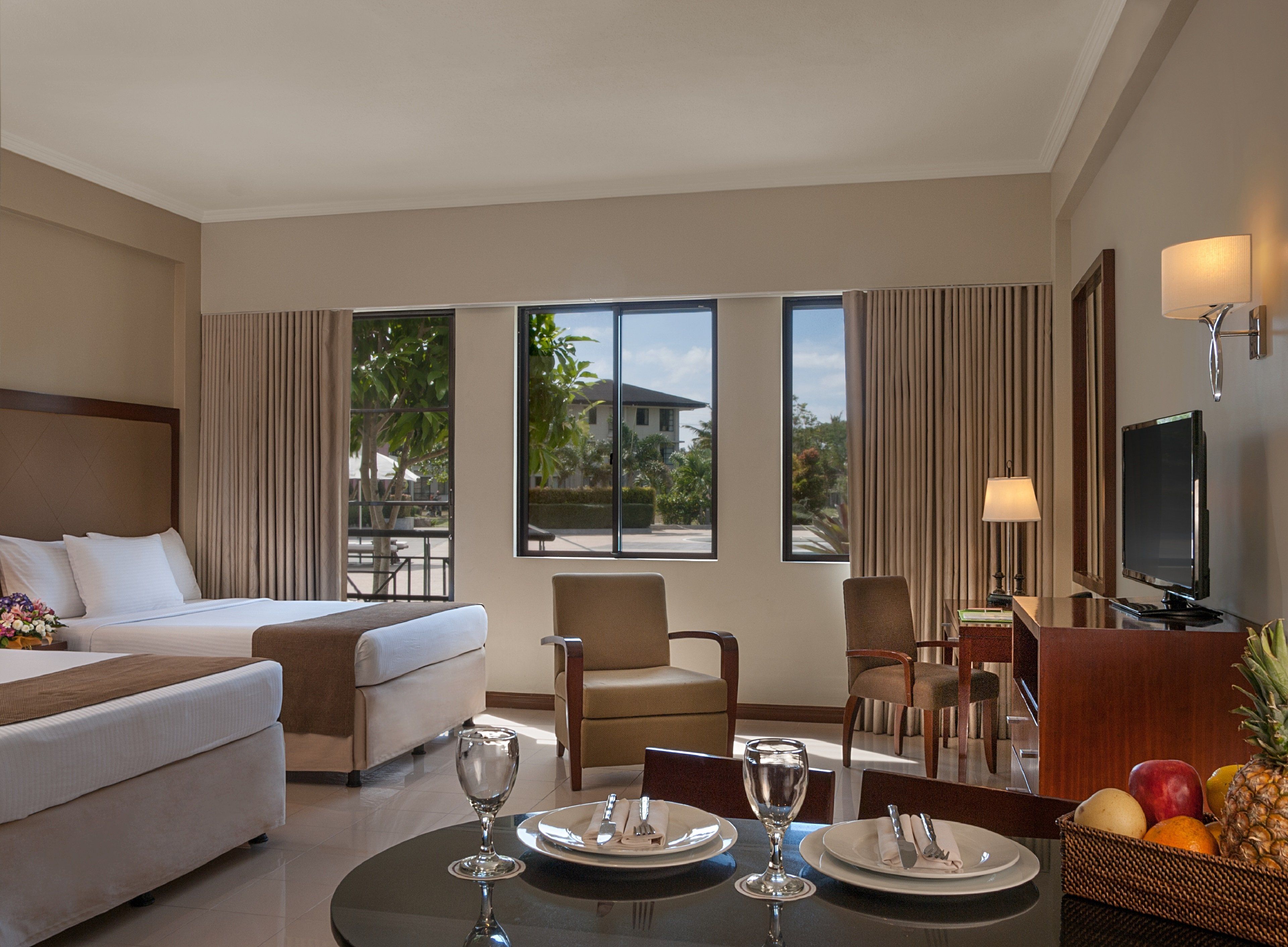 A hotel room with a bed, two armchairs, a dining table set for two, and a television.