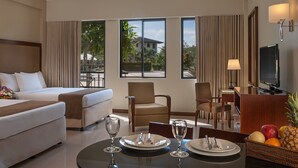 A hotel room with a bed, two armchairs, a dining table set for two, and a television. - Holiday Inn & Suites Batangas Limapark (Malvar)