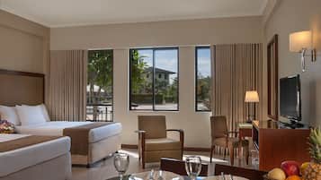 A hotel room with a bed, two armchairs, a dining table set for two, and a television.