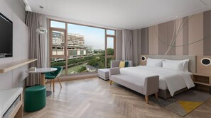 A modern hotel room with a large bed, a seating area, a TV, and a view of the cityscape. - Holiday Inn Dujiangyan Ancient Town (Chengdu)