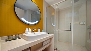 A modern bathroom with a round mirror, a sink, and a glass-enclosed shower. - Holiday Inn Dujiangyan Ancient Town (Chengdu)