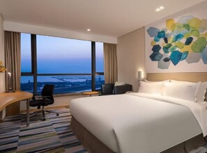 Quarto de hotel com uma cama grande, uma escrivaninha, uma cadeira e vista para a cidade pela janela.