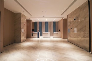 Um hall amplo com piso de mármore, balcão de recepção e um elevador moderno.