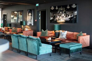 Espaço lounge moderno com sofás, poltronas, área de bar e uma grande foto pendurada na parede.