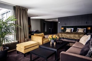 Quarto de hotel moderno com uma cama grande, um sofá, uma mesa de centro e um vaso de plantas.