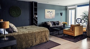 A modern bedroom with a bed, a sofa, a chair, a nightstand, a lamp, and a large window.
