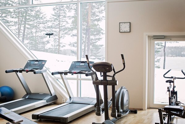A gym with treadmills, an elliptical, and a stationary bike, with a view of snow-covered trees outside.