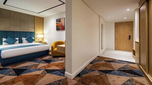 Une chambre d’hôtel avec un lit, un bureau, une chaise, une porte et un tapis à motifs.