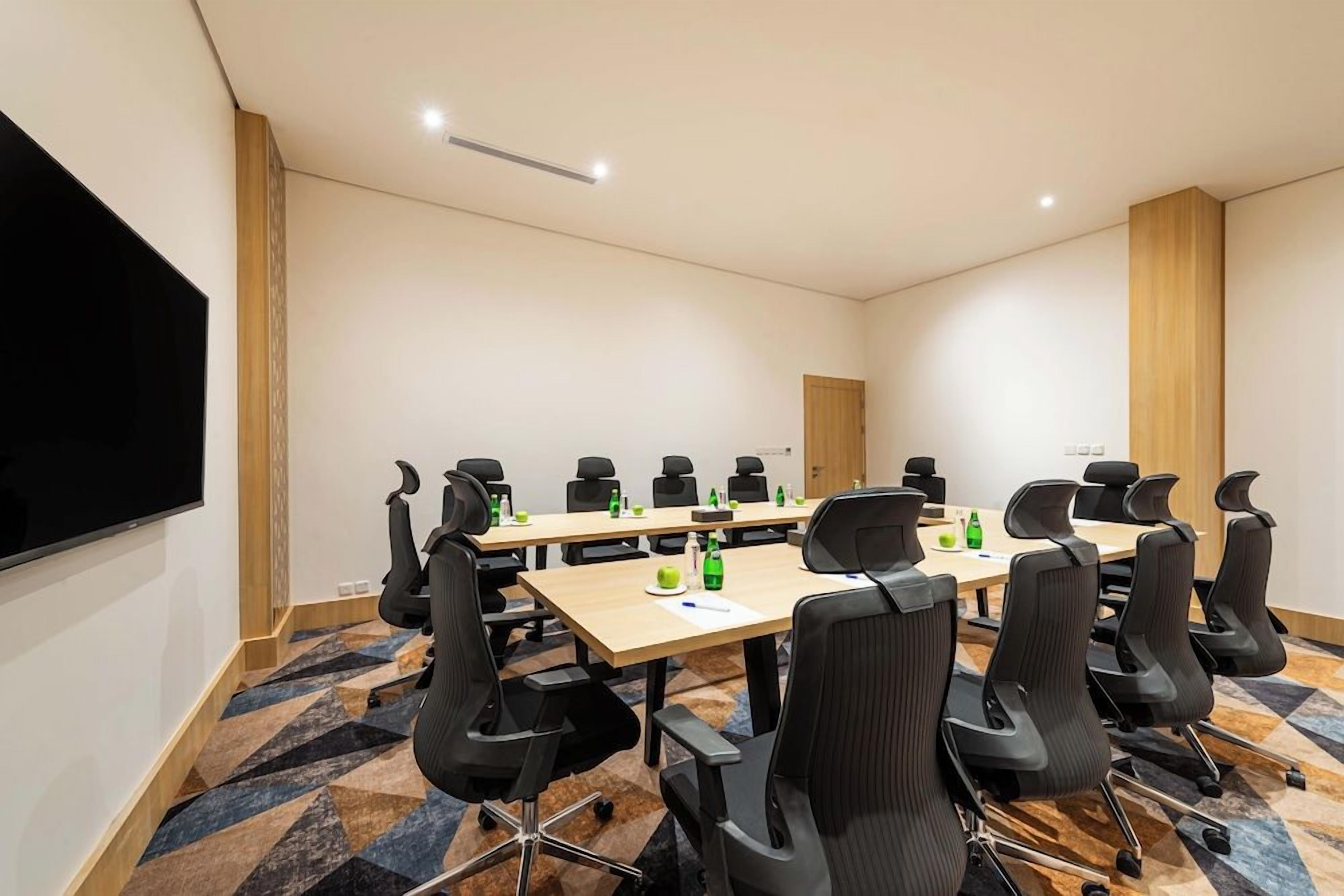A conference room with a long table, black chairs, a flat-screen TV, and a patterned carpet.
