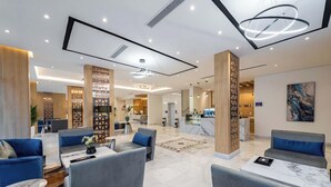 Un hall d’hôtel moderne, doté d’espaces aménagés avec des sièges, d’un comptoir de réception et d’une cuisine ouverte.