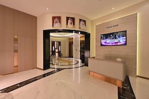 A lobby with a reception desk, a television screen, and a circular decorative floor pattern. - Pavilion Palace Hotel (Sharjah)