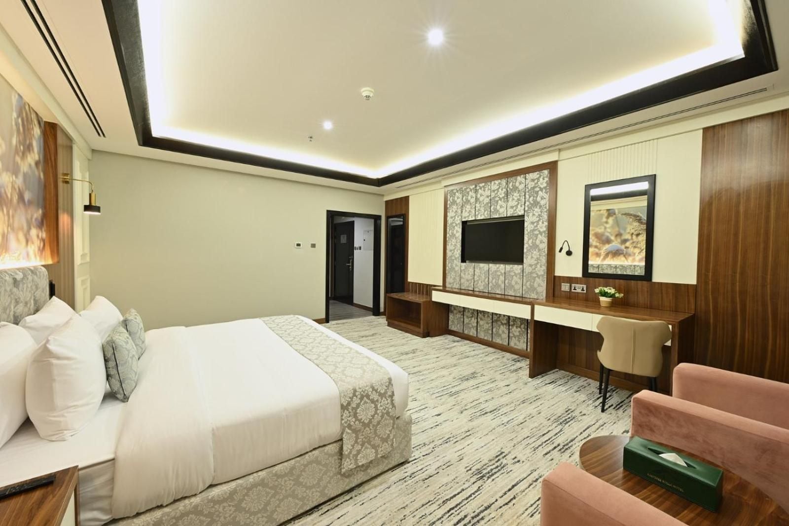 Una habitación de hotel con una cama grande, un escritorio, un televisor montado en la pared y una pequeña zona de estar.