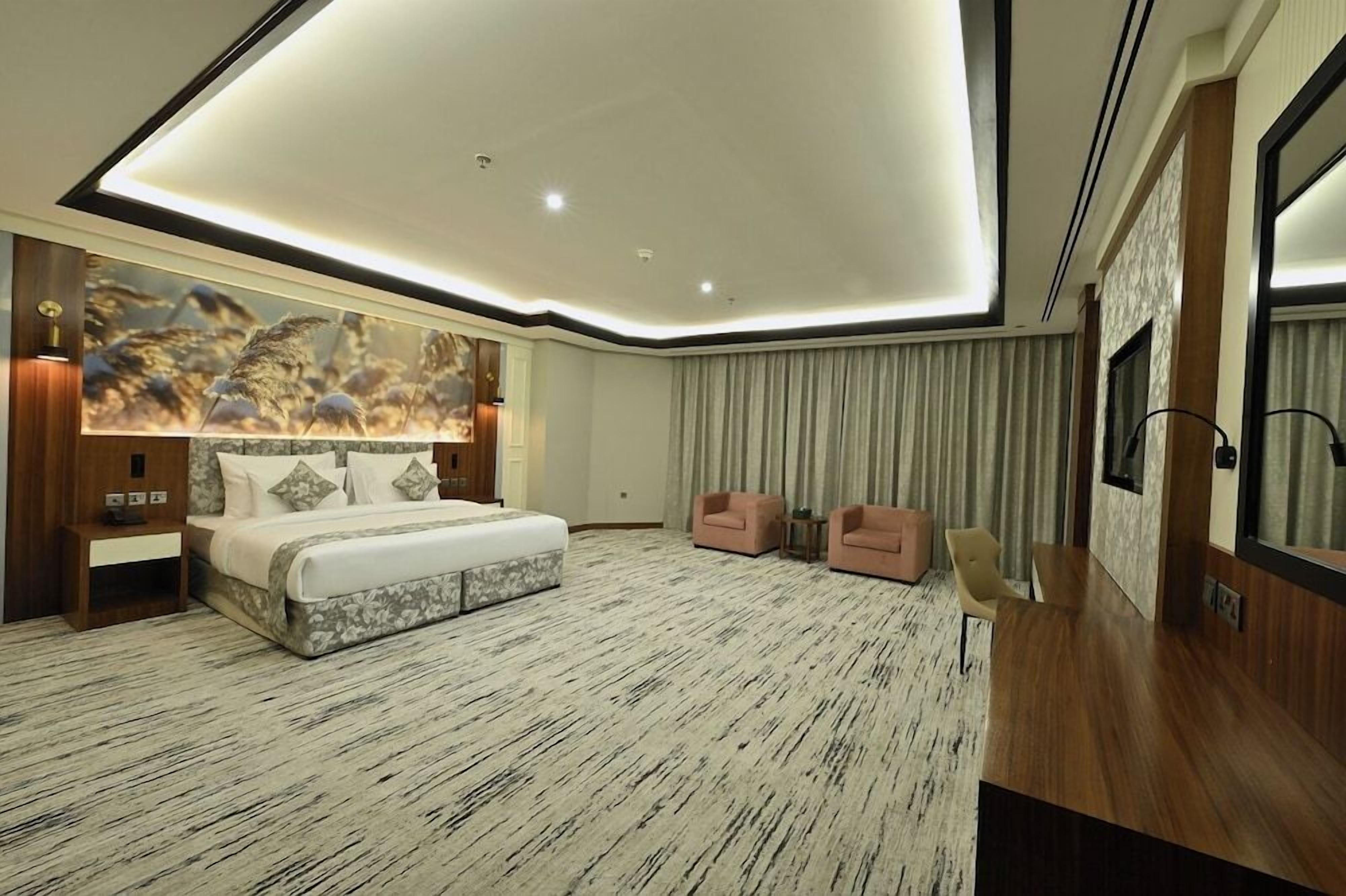 Een moderne hotelkamer met een groot bed, twee fauteuils, een bureau en een grote spiegel.