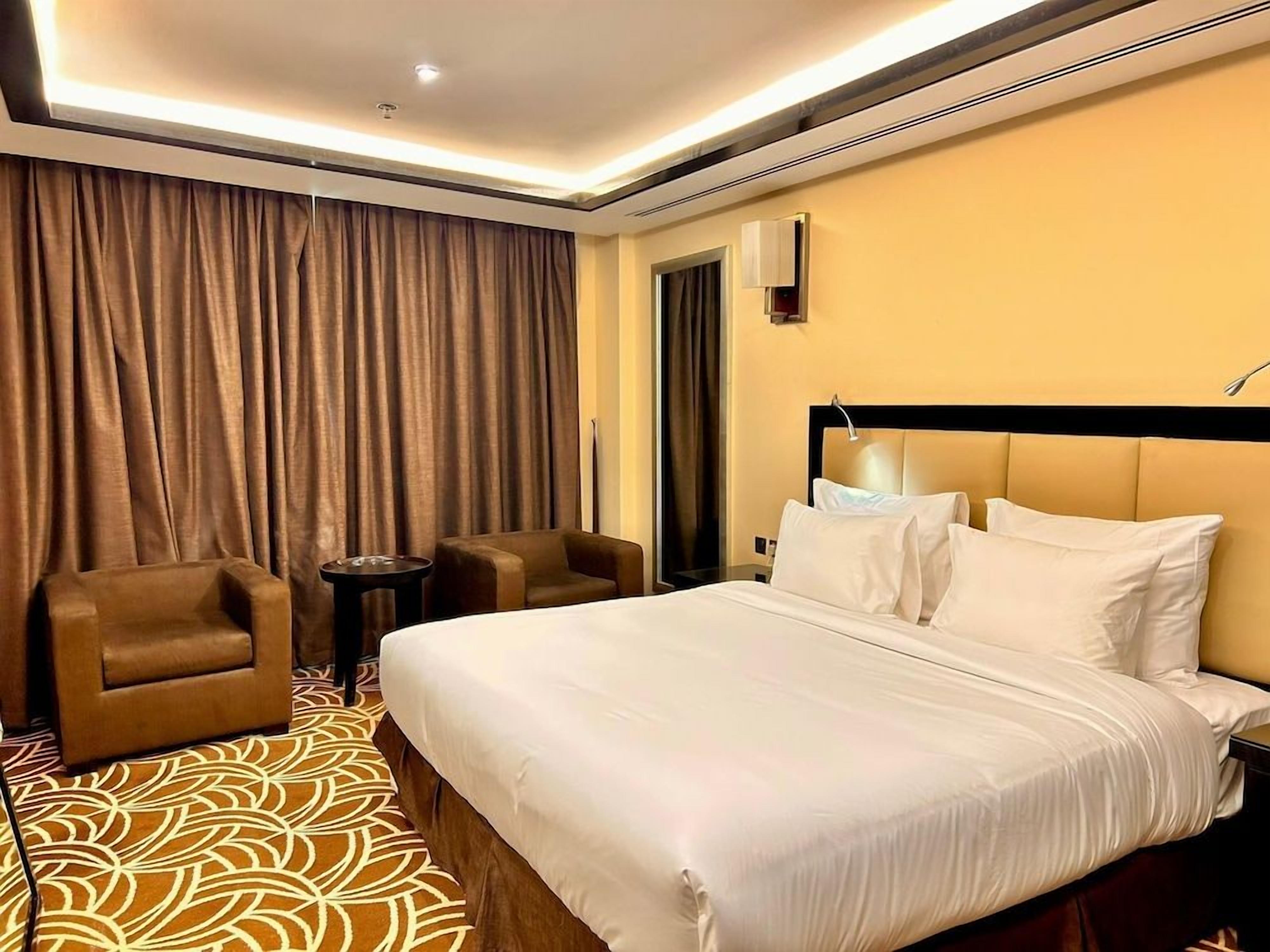 Una habitación de hotel con una cama grande, dos sillones, una mesita y una cortina.