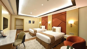 A hotel room with two beds, a desk, chairs, and a minibar. - Pavilion Palace Hotel (Sharjah)