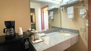 A hotel bathroom with a coffee maker, a mirror, a towel rack, and a hair dryer.