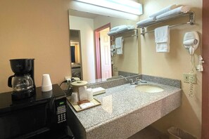 Une salle de bain d’hôtel équipée d’une machine à café, d’un lavabo, d’un miroir et d’un sèche-cheveux.