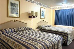 Une chambre d’hôtel avec deux lits, une table de chevet, une lampe et une fenêtre avec des rideaux.