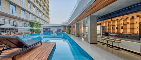 A modern hotel with a swimming pool, outdoor bar, and lounge area.