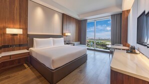 A modern hotel room with a large bed, a desk, and a balcony with a city view. - VM Hotel (Phnom Penh)