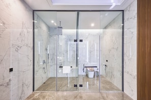 Un baño moderno con ducha acristalada, paredes de mármol y un inodoro a la vista.