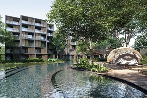 Ein modernes Gebäude mit mehreren Balkonen, einem Wasserspiel und einem großen Baum.