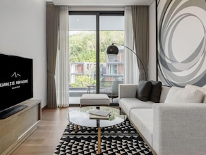 Un salon moderne doté d’un téléviseur à écran plat, d’un canapé, d’une table basse et offrant une vue sur un balcon aménagé avec du mobilier d’extérieur.