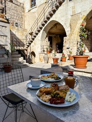 Un espace de restauration en plein air avec une table en pierre, des assiettes remplies de nourriture et un escalier menant à un niveau supérieur.