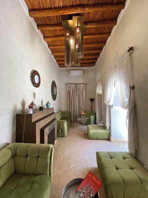 A room with a fireplace, green upholstered chairs, a small table with a book, and a view of the outdoors through a window. - Riad BAB Yacout Piscine and SPA (Marrakech)