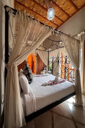 A bed with a canopy, a chandelier, and a view of an outdoor area. - Riad BAB Yacout Piscine & SPA (Marrakech)