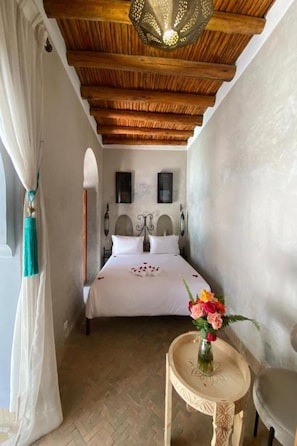 Een slaapkamer met een houten plafond, een bed met witte lakens, een vaas met bloemen en een klein tafeltje.