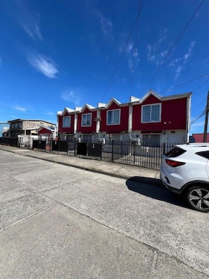 A row of red houses with a white car parked in front. - Departamentos Egaña (Puerto Montt)