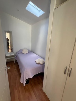A bedroom with a bed, a wardrobe, a small table, and a skylight. - Departamentos Egaña (Puerto Montt)